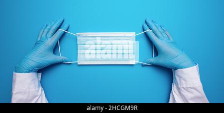 Médecin mains dans des gants montrant un masque médical sur fond bleu.Mesures préventives pour protéger contre l'infection par le virus Covid-19 Corona. Banque D'Images