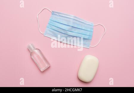 Masque médical bleu, savon et désinfectant pour les mains sur fond rose.Concept de protection contre la pandémie de covid 19 du virus corona. Banque D'Images