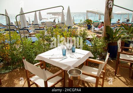 Table et chaises sur table avec verres, couverts et serviette blanche dans un restaurant chic au bord de la mer. Banque D'Images