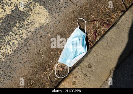 Un masque chirurgical jeté allongé dans un caniveau poussiéreux.Au cours de la COVID, de nombreux masques faciaux ont été perdus ou jetés. Banque D'Images