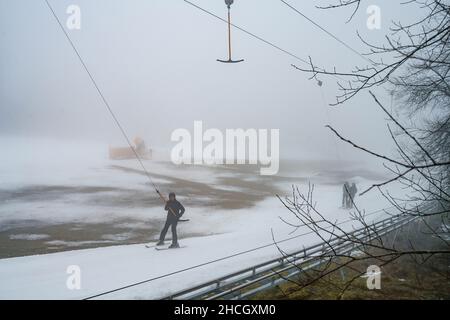 Abtsroda, Allemagne.29th décembre 2021.Les skieurs utilisent la remontée mécanique de conte de fées sur la pente de la Wasserkuppe.À des températures supérieures au point de congélation, les sports d'hiver étaient encore possibles sur la pente de neige artificielle, alors que les prairies brunes prédominent tout autour.Credit: Frank Rumpenhorst/dpa/Alay Live News Banque D'Images