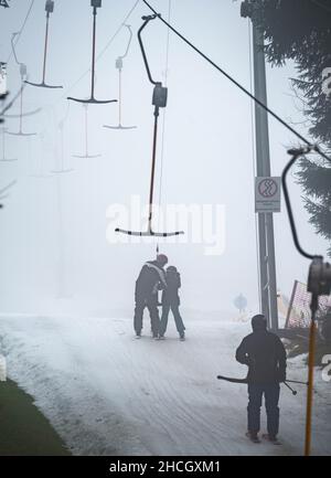 Abtsroda, Allemagne.29th décembre 2021.Les skieurs utilisent la remontée mécanique de conte de fées sur la pente de la Wasserkuppe.À des températures supérieures au point de congélation, les sports d'hiver étaient encore possibles sur la pente de neige artificielle, alors que les prairies brunes prédominent tout autour.Credit: Frank Rumpenhorst/dpa/Alay Live News Banque D'Images