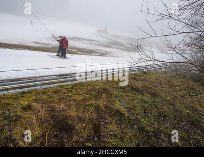 Abtsroda, Allemagne.29th décembre 2021.Les skieurs utilisent la remontée mécanique de conte de fées sur la pente de la Wasserkuppe.À des températures supérieures au point de congélation, les sports d'hiver étaient encore possibles sur la pente de neige artificielle, alors que les prairies brunes prédominent tout autour.Credit: Frank Rumpenhorst/dpa/Alay Live News Banque D'Images