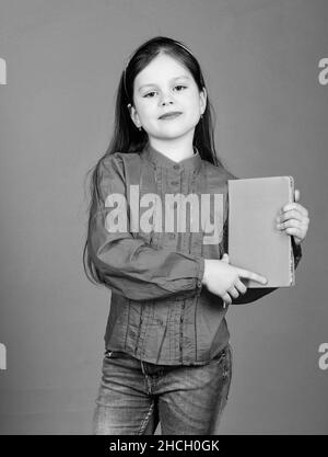 Confiant dans ses connaissances.Adorable petite fille tenant livre avec couverture orange.Mignon petit enfant avec la connaissance du livre dans les mains.Connaissances et compétences Banque D'Images