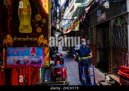 Un homme âgé pousse un transporteur de marchandises vide le long d'une ruelle étroite dans le quartier chinois de Bangkok, en Thaïlande Banque D'Images