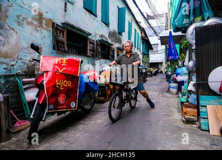 Une femme âgée fait du vélo une longue allée étroite à Talat Noi, Bangkok, Thaïlande Banque D'Images