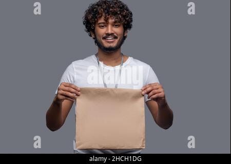 Joyeux homme avec un paquet posant sur le fond gris Banque D'Images