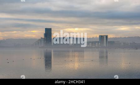 Immeubles d'appartements reflétés dans l'eau de la baie de Cardiff, pays de Galles. C'est un jour d'hivers brumeux Banque D'Images