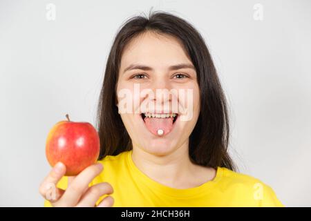 Une femme tient dans sa main une pomme, un comprimé blanc de vitamines ou de suppléments alimentaires sur la langue. Banque D'Images