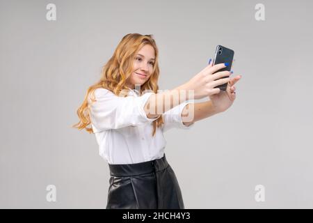 Gros plan jeune blond s'amuser ravie excitée excitée 20s femme en chemise blanche rend un selfie sur un téléphone mobile heureux sourire isolé sur un fond gris clair portrait de studio Banque D'Images