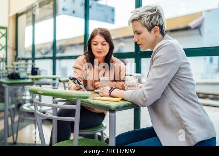 Deux femmes discutant et montrant quelque chose au téléphone dans le café à la gare, Portugal Banque D'Images