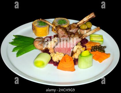 Selle d'agneau torréfiée rose sur polenta de maïs avec oignons rouges et divers légumes, photographie en studio avec fond noir Banque D'Images