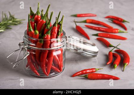 Piment rouge vif dans un pot en verre et dispersé sur une surface grise avec une texture en plâtre.Mise au point sélective. Banque D'Images