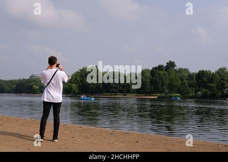 Jeune homme avec dos à l'appareil photo photographier des bateaux de plaisance sur le Hyde Park Serpentine Londres UK. Banque D'Images