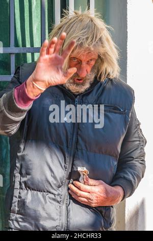 Homme sans-abri gestant tout en tenant l'emballage de son snack Banque D'Images