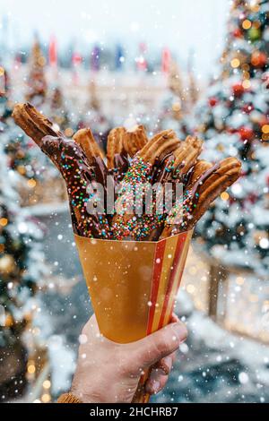 Gaufres churos dans la main sur le marché de la neige d'hiver.Churros cuisine mexicaine de rue dessert.Bonbons fast-food, biscuits de Noël.Photo de haute qualité Banque D'Images