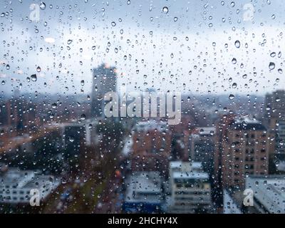 Cliché flou de gouttes de pluie sur une fenêtre contre l'arrière-plan des bâtiments Banque D'Images