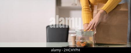 Gros plan des mains des femmes sortez les aliments dans des plateaux jetables d'un sac en papier et placez-les sur la table.Sans visage.Baner. Banque D'Images