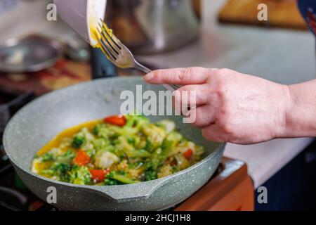 les mains des femmes ajoutent un jaune d'œuf brouillés à la cuisson des légumes tout en cuisinant l'omelette Banque D'Images