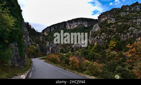 Vue sur la route de campagne pavée D177 traversant un canyon rocheux dans les montagnes rurales du Vaucluse près de Gordes, France en Provence par temps nuageux. Banque D'Images