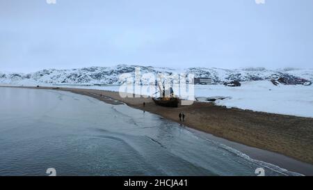 Vue aérienne des vieux navires rouillés laissés sur la rive sablonneuse près de la rive océanique en hiver.Survolant les personnes qui marchent sur la plage près de l'Ocea froid Banque D'Images