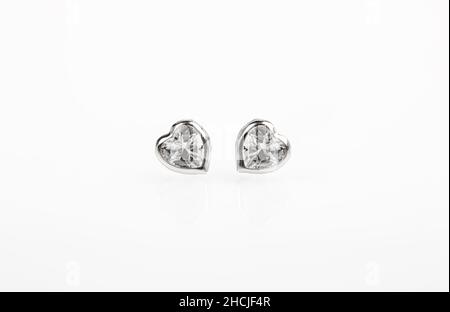 Puces d'oreilles argentées en forme de coeurs sur fond blanc. Banque D'Images