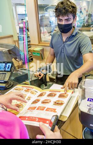 Miami Beach Florida North Beach Denny's Restaurant à l'intérieur hispanique homme hôte aidant le client à choisir le menu comptoir portant un masque facial Banque D'Images