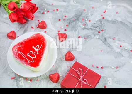 Gâteau en forme de coeur entouré de bougies, boîte cadeau et fleurs sur fond de marbre festif.Concept de la Saint-Valentin.Copier l'espace Banque D'Images