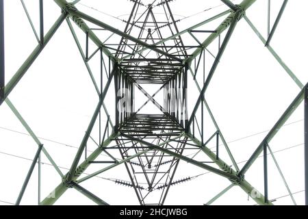 Photographie regardant à l'intérieur à travers une grande tour de transmission électrique en acier contre un ciel gris nuageux Banque D'Images