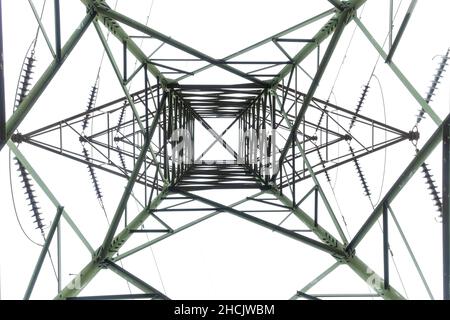 Photographie regardant à l'intérieur à travers une grande tour de transmission électrique en acier contre un ciel gris nuageux Banque D'Images