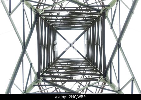 Photographie regardant à l'intérieur à travers une grande tour de transmission électrique en acier contre un ciel gris nuageux Banque D'Images