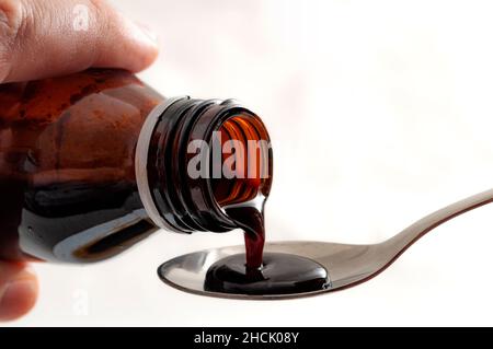 Traitement contre le rhume et la grippe et concept de médecine amère avec gros plan sur les mains verser le sirop contre la toux d'une bouteille de verre brun dans une cuillère à café isolée sur le merlu Banque D'Images