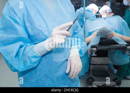 Gros plan de la main d'un chirurgien tenant un scalpel.Mise au point sélective.Un chirurgien avec un scalpel en gants uniformes et stériles dans la salle d'opération. Banque D'Images