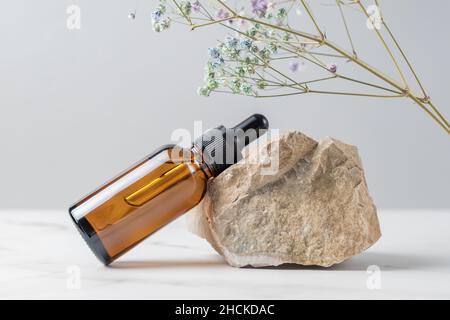 Faire face au sérum ou à l'huile essentielle dans un flacon compte-gouttes en verre foncé près de la pierre et de la branche séchée de la fleur de gitsophila.Cosmétiques pour le soin de la peau. Présentation du produit Banque D'Images