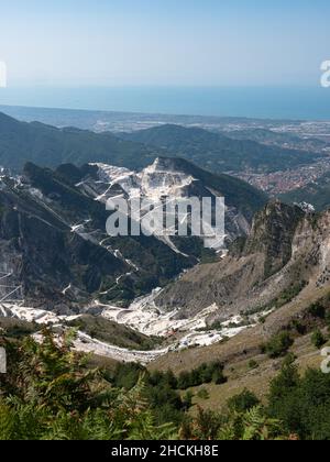 Vue sur les carrières de marbre de Carrare, les chemins sculptés sur le flanc de la montagne et la ville de Carrare et la côte en face. Banque D'Images