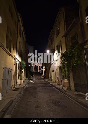 Vue de nuit sur une ruelle étroite dans le centre historique de la ville d'Arles, Provence, France avec de vieux bâtiments traditionnels, des lumières de rue et un amphithéâtre romain. Banque D'Images