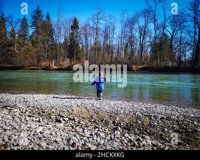 mignon petit garçon de cinq ans jetant des pierres à l'eau à l'extérieur lors d'une journée d'été Banque D'Images