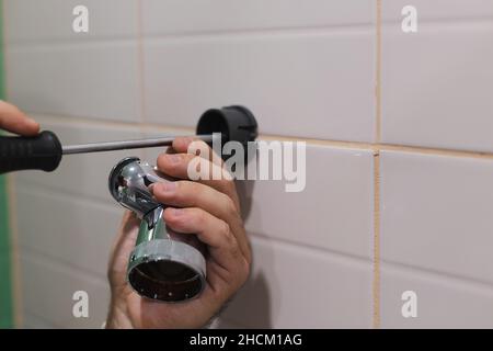 Gros plan des mains de l'homme installant le support de la pomme de douche avec un tournevis sur le mur carrelé des toilettes pendant les travaux de rénovation dans la salle de bains.Saleté de Banque D'Images