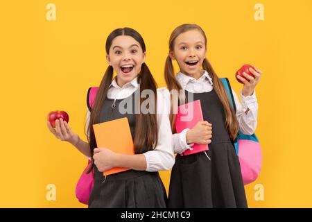 Les enfants heureux en uniforme d'école tiennent des livres et des pommes pour manger sainement repas d'école, snack Banque D'Images