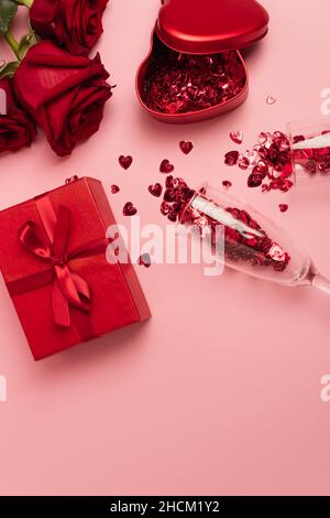 vue de dessus des verres à champagne avec des coeurs confettis près des boîtes-cadeaux et des roses rouges sur le rose Banque D'Images