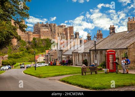 Les touristes et vacanciers, le long de la rue principale dans le village de Northumberland England Royaume-Uni Bamburgh avec château de Bamburgh en arrière-plan Banque D'Images