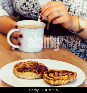 Gros plan d'une femme qui boit du café et qui mange du beurre d'arachide et de la confiture sur un bagel Banque D'Images