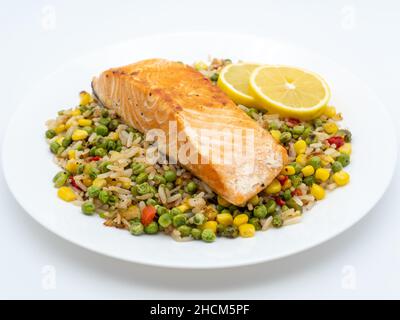 Gros plan d'un steak de saumon sur du riz avec des légumes et deux morceaux de citron sur une assiette blanche Banque D'Images