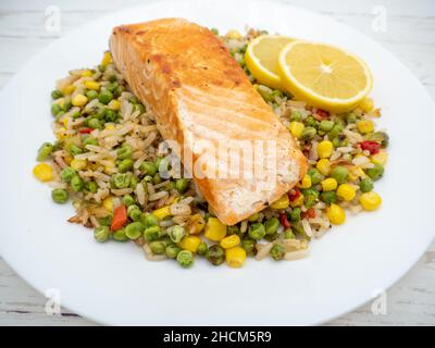 Gros plan d'un steak de saumon sur du riz avec des légumes et deux morceaux de citron sur une assiette blanche Banque D'Images