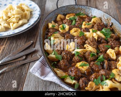 Boulettes de viande avec pâtes. Délicieux plat de meatball salé avec tortellini dans une sauce aux champignons bruns. Servi dans une lèchefrite sur une table en bois. Banque D'Images