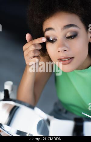 Blogueur afro-américain souriant appliquant le maquillage près du miroir et du téléphone portable Banque D'Images