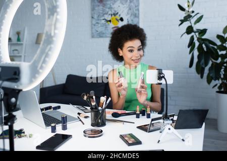 Un blogueur afro-américain souriant tenant face à des fondations près d'un smartphone à la maison Banque D'Images