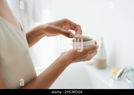 Vue rognée d'une femme afro-américaine tenant un pot avec des taches oculaires dans la salle de bains Banque D'Images