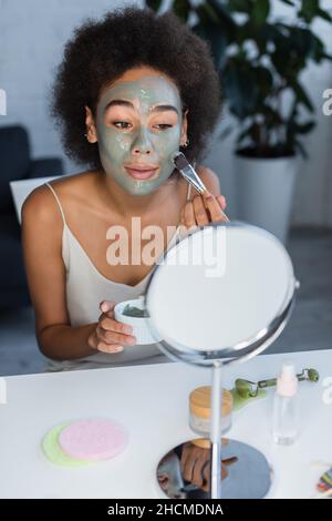 Femme afro-américaine appliquant un masque près du miroir et du rouleau de jade à la maison Banque D'Images