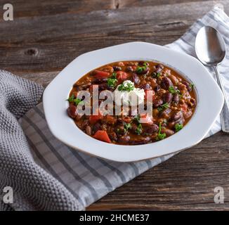 Assiette avec Chili frais cuit con carne isolée sur fond de table en bois. Surmontée de crème aigre Banque D'Images